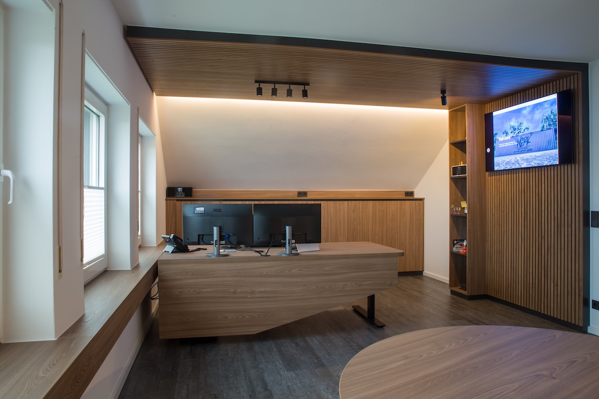 Moderner Arbeitsplatz mit maßgefertigtem Holzschreibtisch, integrierter Technik und indirekter Beleuchtung im Büro