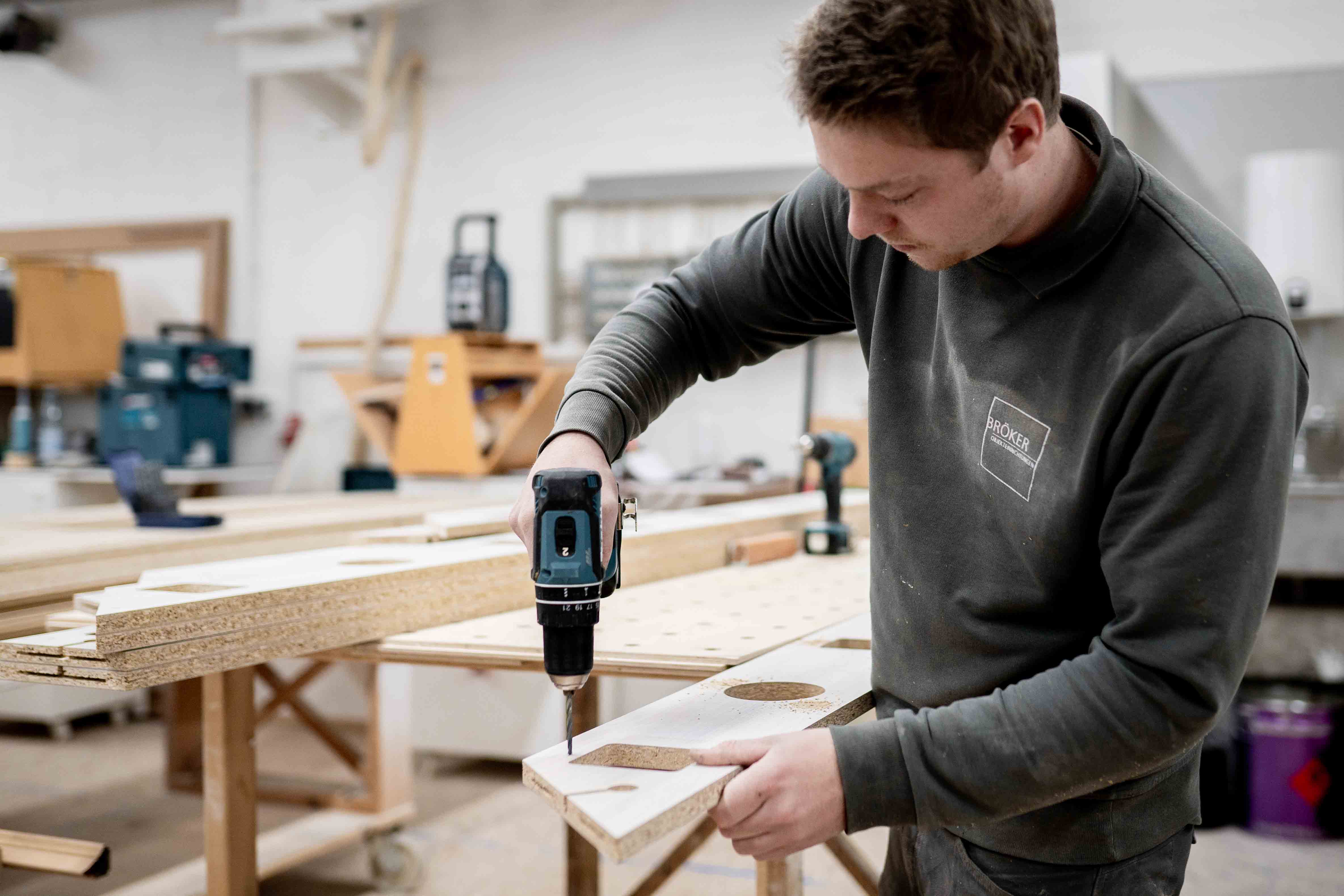Mitarbeiter bohrt ein Loch in ein Holzbauteil an einer Werkbank