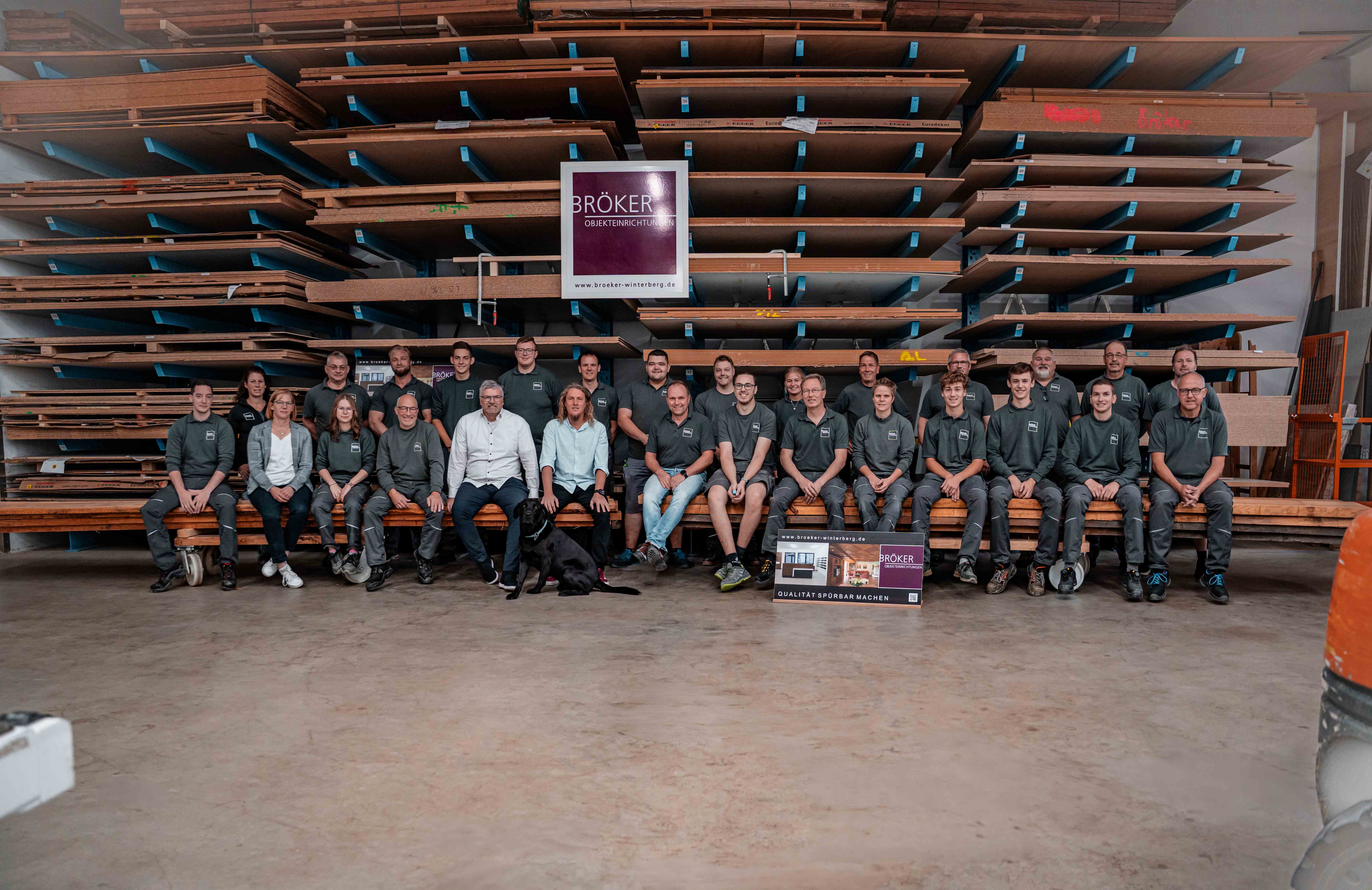 ruppenfoto der Mitarbeitenden vor einem großen Holzlager in der Werkhalle