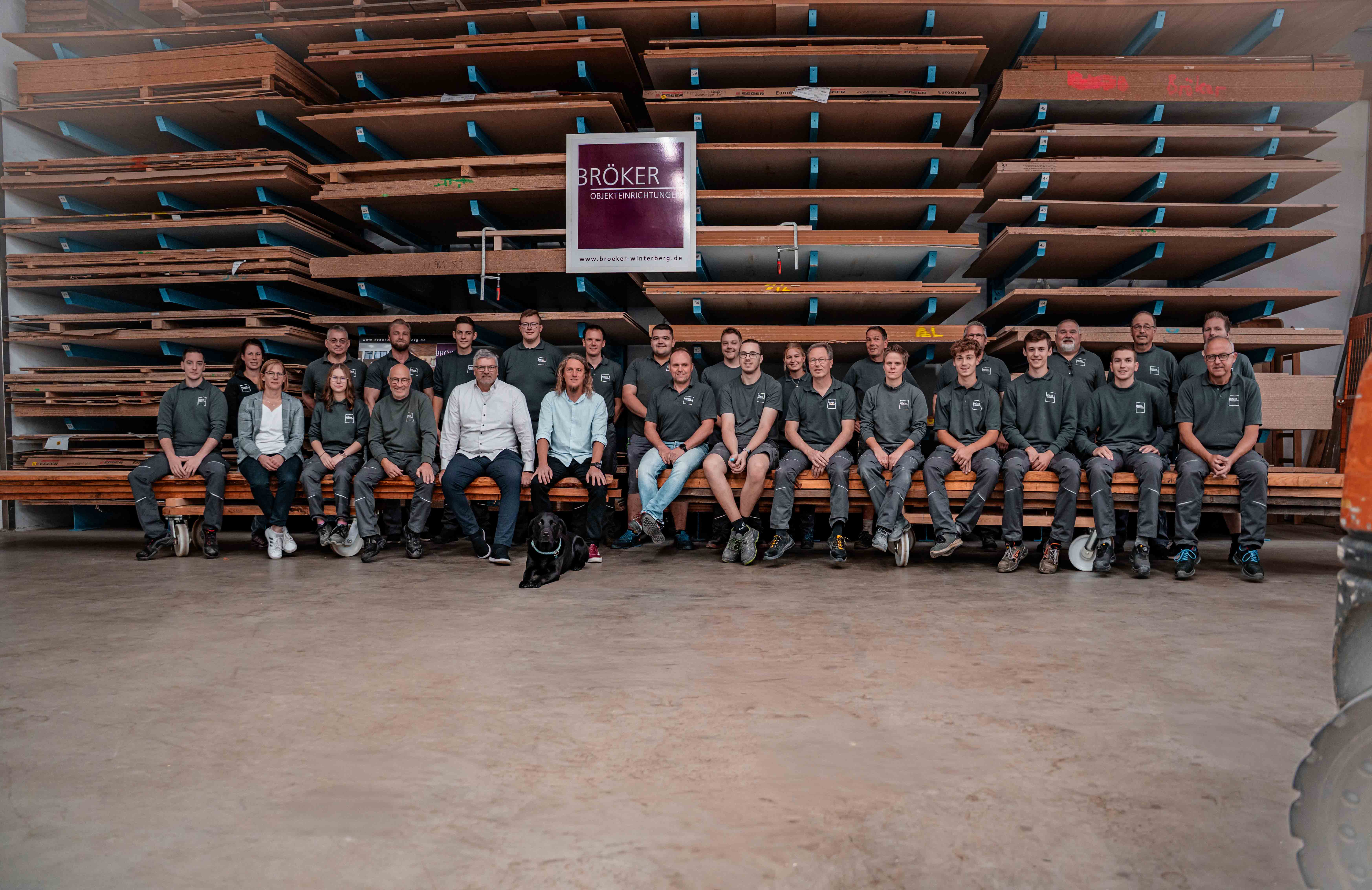 Mannschaftsfoto der Mitarbeitenden in der Werkstatt mit Holzregalen im Hintergrund