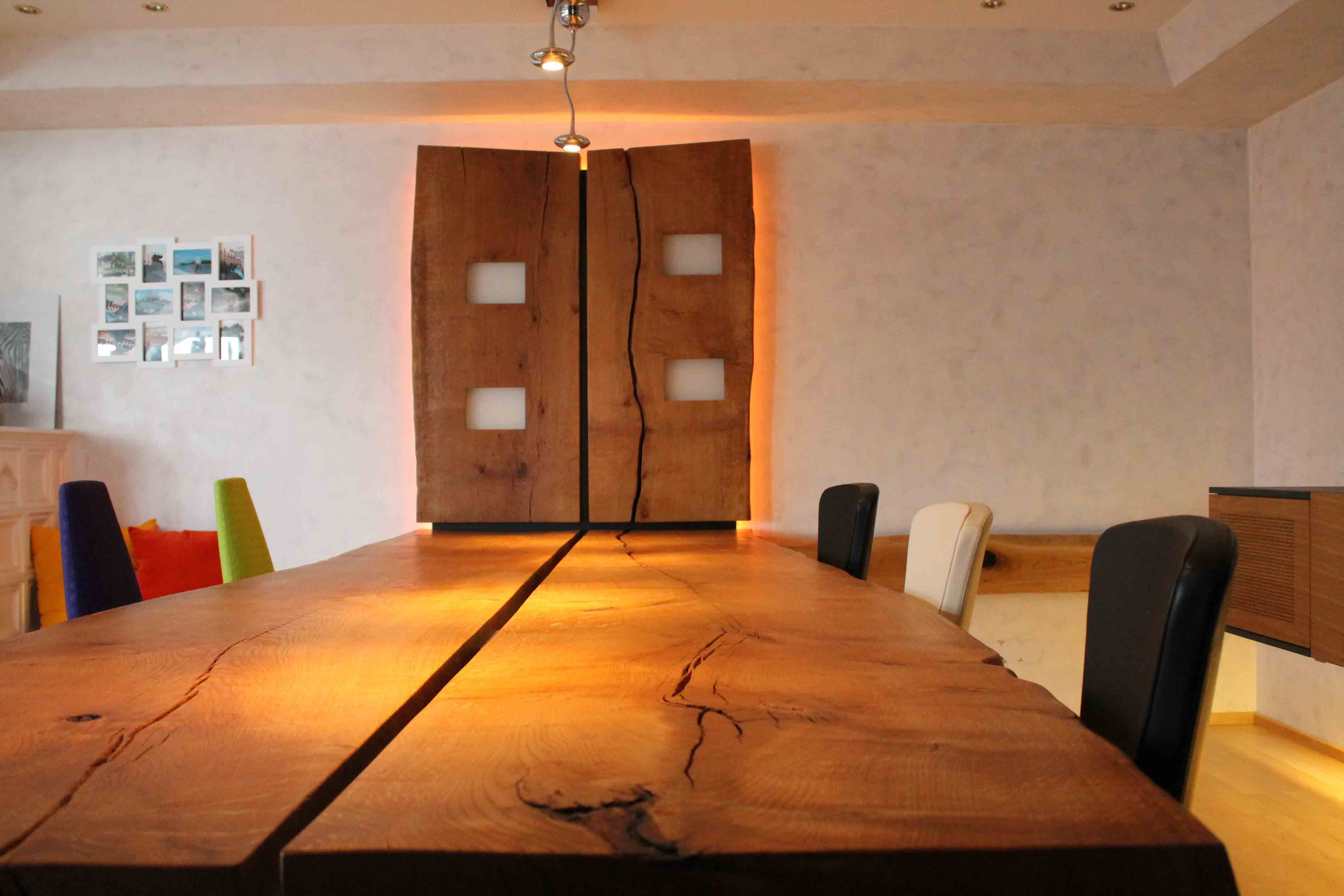 Großer Massivholz-Esstisch mit natürlicher Maserung und markanter Holzfuge, umgeben von unterschiedlich farbigen Stühlen.