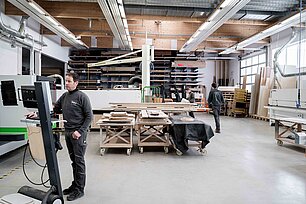 Mehrere Mitarbeiter arbeiten in der Werkhalle von Bröker Objekteinrichtungen mit Holzplatten und Maschinen