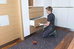 Handwerker kniet vor einem Möbelstück und montiert eine Schublade