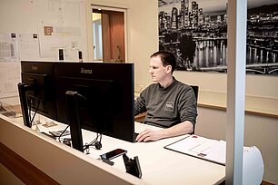 Mitarbeiter arbeitet an einem Schreibtisch mit mehreren Monitoren in dem Büro von Bröker