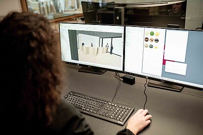 Person arbeitet an zwei Monitoren mit einer dreidimensionalen Innenraumvisualisierung