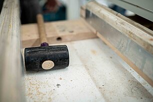 Gummihammer liegt auf einer Werkbank neben Holz- und Metallteilen